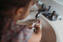 Petite fille se lave les mains dans l'évier de salle de bain avec savon. — Photo de stock