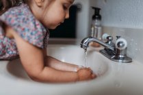Маленька дівчинка миє руки у ванній раковині з милом . — стокове фото