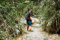 Giovane uomo escursioni lungo il fiume circondato da piante verdi in estate — Foto stock