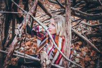 Portrait girl with blond hair and blue eyes amid branches in a wood — Stock Photo