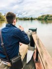 Человек выпивает бокал шампанского на лодке, глядя на реку — стоковое фото