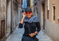 Жінка в бейсбольній шапці та помаранчевих сонцезахисних окулярах на вуличній алеї — стокове фото