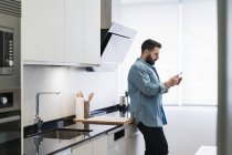 Uomo con un telefono cellulare in cucina in camicia di jeans — Foto stock