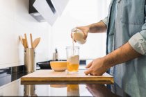 Ein Mann in Jeanshemd kocht in der Küche. Mann gießt Milch in einen Behälter — Stockfoto