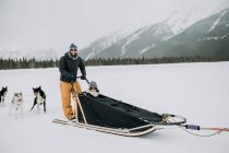 Man and woman couple sit and stand in dogsled in canadian rockies — Stock Photo