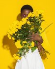 Attraktive schwarze Frau mit kurzen Haaren mit gelben Blüten auf gelbem Hintergrund — Stockfoto