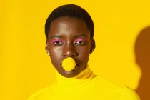 Attraente donna africana con fiore giallo in bocca e rosa compongono isolato su sfondo giallo — Foto stock