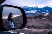 Молода жінка дивиться на захід сонця в горах, відображених у дзеркалі — стокове фото