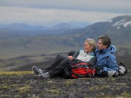 Pareja de senderismo relajándose en la ladera de la montaña en Islandia - foto de stock