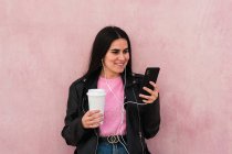 Mujer joven escuchar música y mira su teléfono inteligente en una espalda rosa - foto de stock