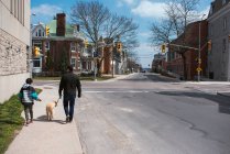 Father and son walking a dog on the sidewalk of a quiet city street. — Stock Photo