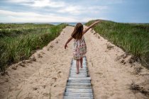 Uma menina em um vestido branco caminha ao longo do caminho na praia — Fotografia de Stock