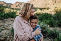 Mãe abraçando sorrindo criança não binária no deserto — Fotografia de Stock