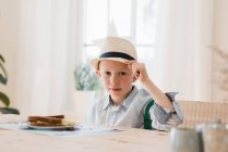 Menino sentou-se comendo seu café da manhã vestido inteligentemente com um chapéu — Fotografia de Stock
