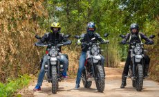 Tres amigos montando sus motocicletas scrambler a través de Forrest - foto de stock