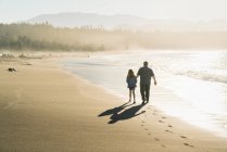 Батько і дочка гуляють уздовж пляжу на заході сонця — стокове фото