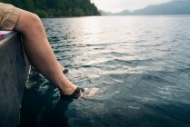 Los pies del hombre en sandalias sumergidas en el lago - foto de stock