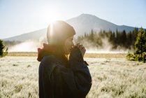 Young woman drinking coffee at sunrise near foggy mountain — Stock Photo