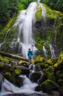 Young woman looking up at huge waterfall in forest — Stock Photo
