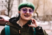 Retrato de hipster feliz não-binário em óculos de sol roxos em pé na cidade — Fotografia de Stock