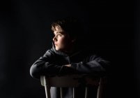 Portrait discret d'un adolescent assis sur une chaise dans une pièce sombre. — Photo de stock