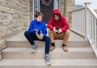 Dos adolescentes sentados y hablando en los escalones de una casa. - foto de stock