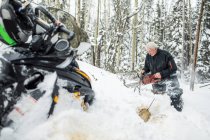 Anciano retirado usando motosierra para despejar senderos mientras motos de nieve. - foto de stock
