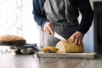 Uomo che taglia il pane con un coltello su sfondo bianco — Foto stock