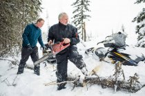 Homem aposentado e seu filho usando motosserra para limpar trilhas enquanto snowmobiling — Fotografia de Stock