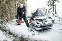 Homem aposentado usando motosserra para limpar trilhas enquanto snowmobiling — Fotografia de Stock