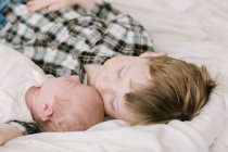 Старший брат и его новорожденная младшая сестра прижимаются к кровати — стоковое фото
