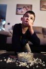 A kid eats popcorn at home while watching a movie — Stock Photo