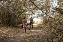 Uomini con tavole da surf che camminano nella foresta di bambù — Foto stock
