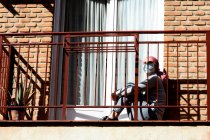 Una mujer con cáncer y depresión encerrada en su balcón. Pañuelo rosa y mascarilla. Coronavirus cuarentena. - foto de stock