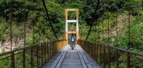 Homme conduisant une moto de tourisme sur un pont suspendu au Pérou — Photo de stock
