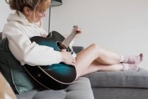 Жінка сиділа на дивані, граючи на гітарі посміхаючись — стокове фото