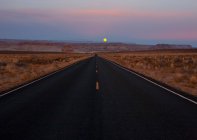 Desert road at dusk with moonrise, Arizona, USA — Stock Photo