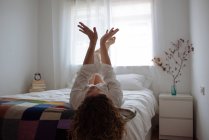 Mulher de cabelos encaracolados deitada na cama brincando com as mãos — Fotografia de Stock