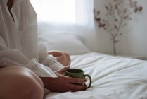 Großaufnahme von Händen, die eine Tasse Kaffee auf dem Bett halten — Stockfoto