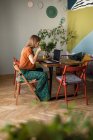 Mujer con taza de té de vidrio trabaja en línea en casa por ordenador portátil en la mesa - foto de stock
