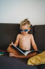 Jeune homme tout-petit lisant seins nus avec des lunettes pour l'école à domicile — Photo de stock