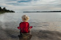 Kleines Mädchen sitzt an einem Sommertag im Stuhl am Strand — Stockfoto