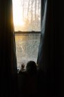 Маленькая девочка смотрит на закат через окно.. — стоковое фото