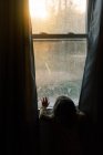 Petite fille regardant le coucher du soleil à travers une fenêtre. — Photo de stock