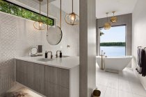 Потрясающая ванная комната в новом современном стиле роскошный дом с двойным тщеславием, плитка, пол, подвесные огни, ванна с удивительным видом на внешний вид воды — стоковое фото