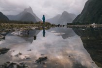 Young woman stands at the view of Mitre Peak in Milford Sound, New Zealand — Stock Photo
