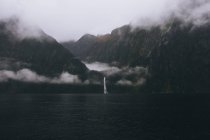 Szenische Ansicht des Wasserfalls gegen Berge am Milford Sound bei nebligem Tag, Neuseeland — Stockfoto