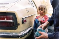 Father and his toddler daughter washing a classic car together — Stock Photo