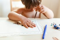 Sem camisa menino sentado na mesa desenho em casa — Fotografia de Stock