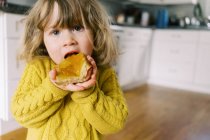 Kleines Mädchen genießt frisch gebackenes Brot mit Marillenmarmelade. — Stockfoto